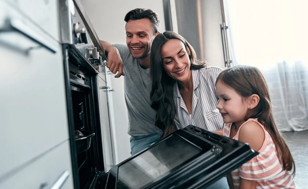 happy-young-family-with-their-little-cute-daughter-are-peep-into-oven-while-cooking-cakes-kitchen-min